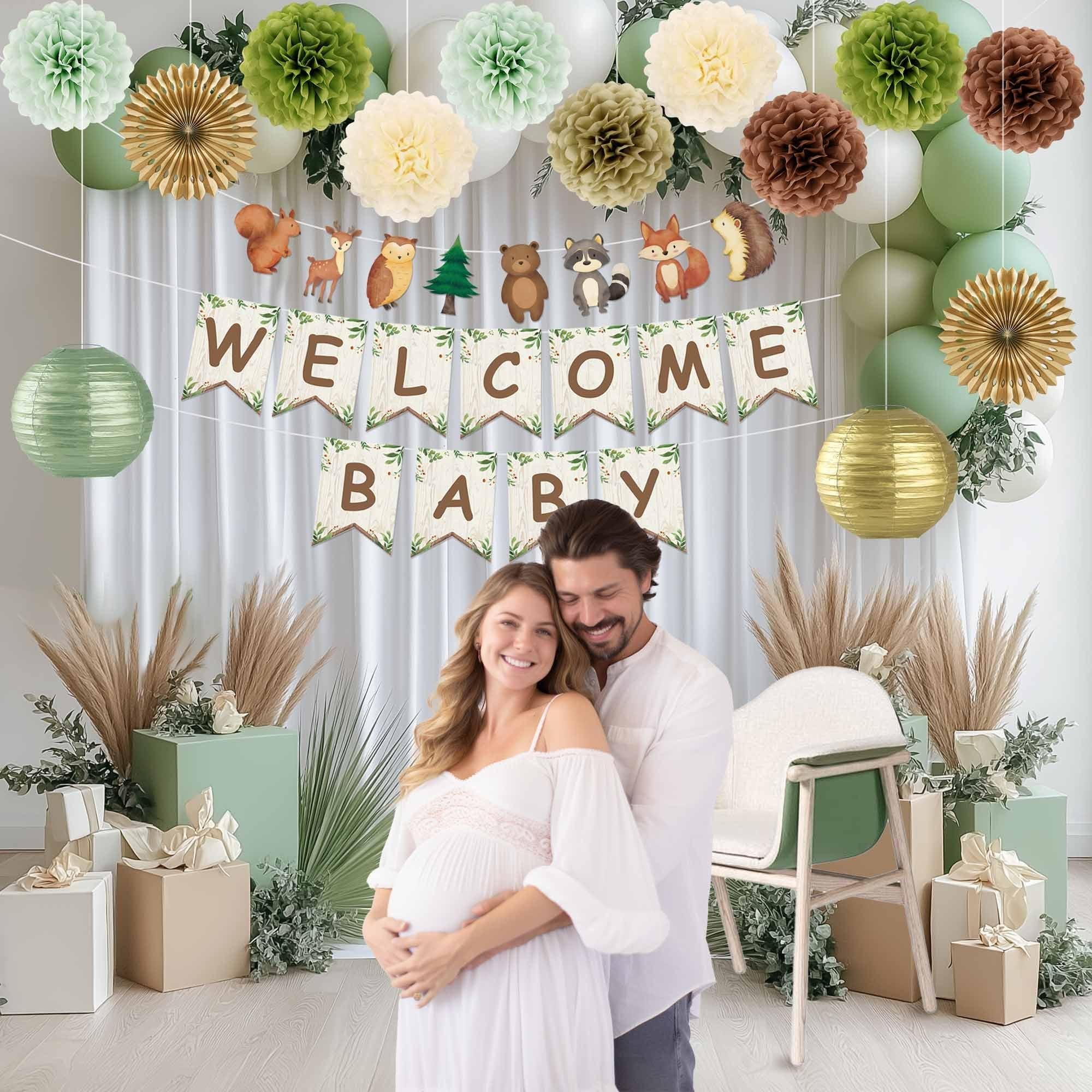 Couple celebrating a baby shower with woodland-themed decorations including a 'Welcome Baby' banner, pom poms, and balloons.