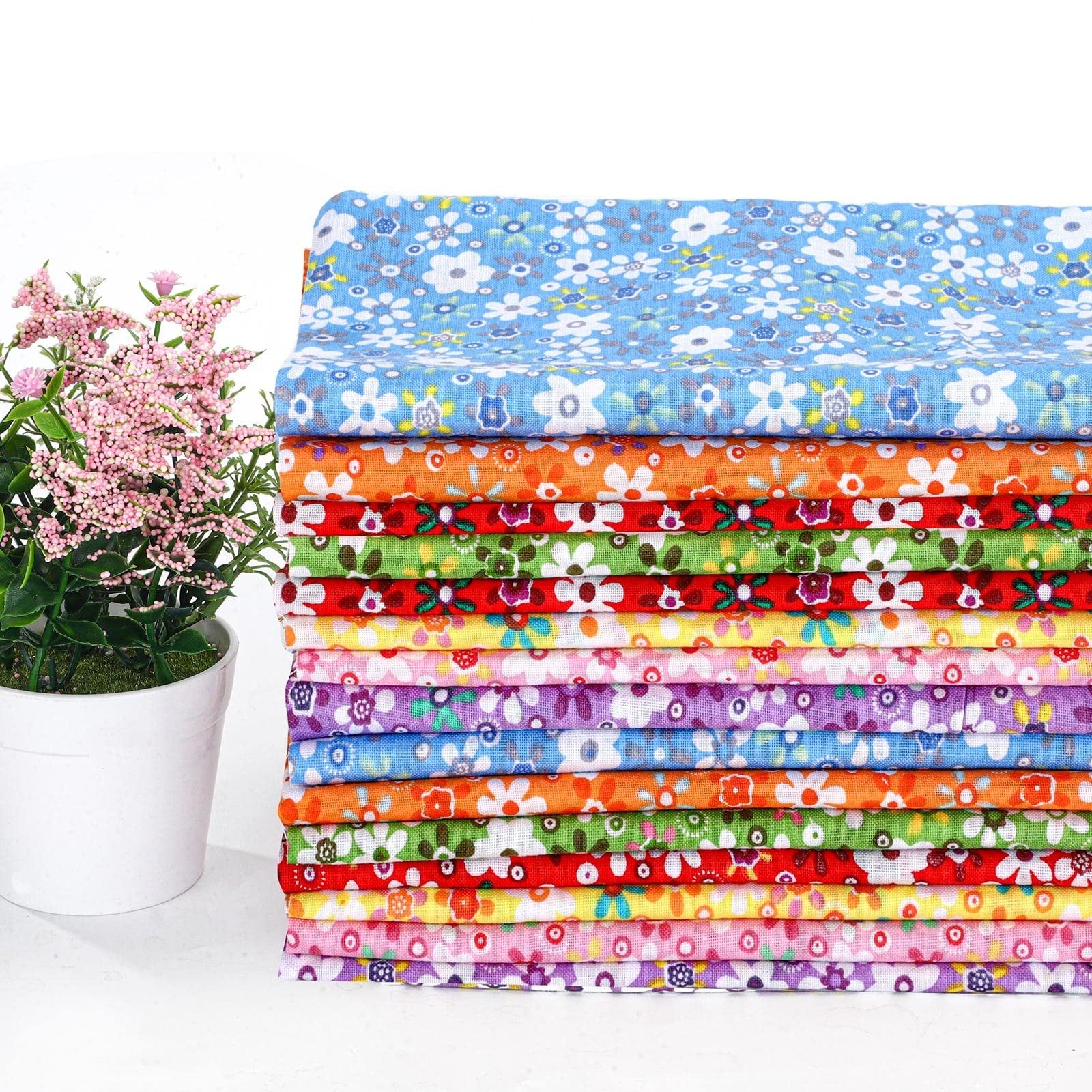 Stack of 15 colorful floral fabric squares with a potted pink plant on the left.