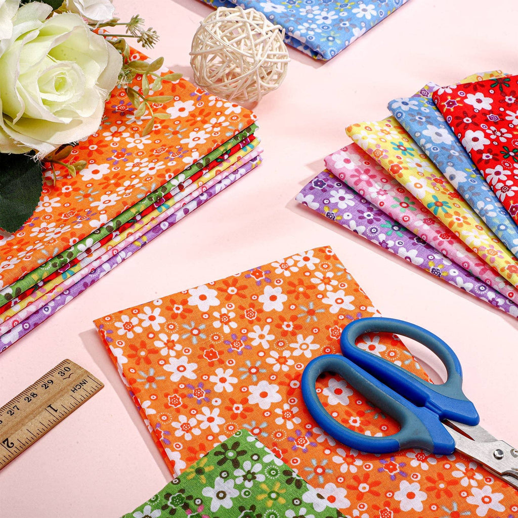 Stack of floral fabric squares with scissors and ruler on pink background