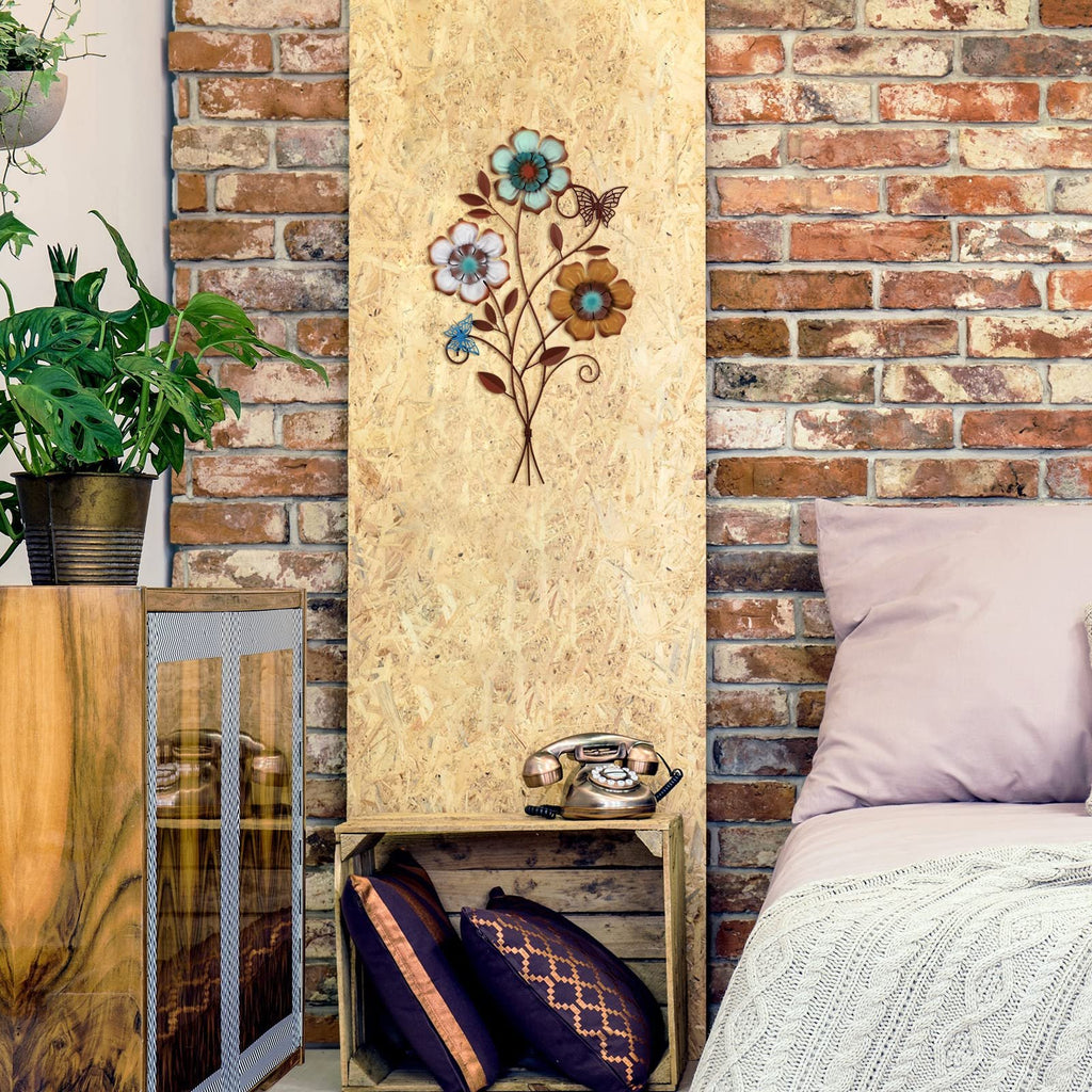 Tricolor metal flower wall decor with butterflies mounted on a wood panel, next to a bed and plant.