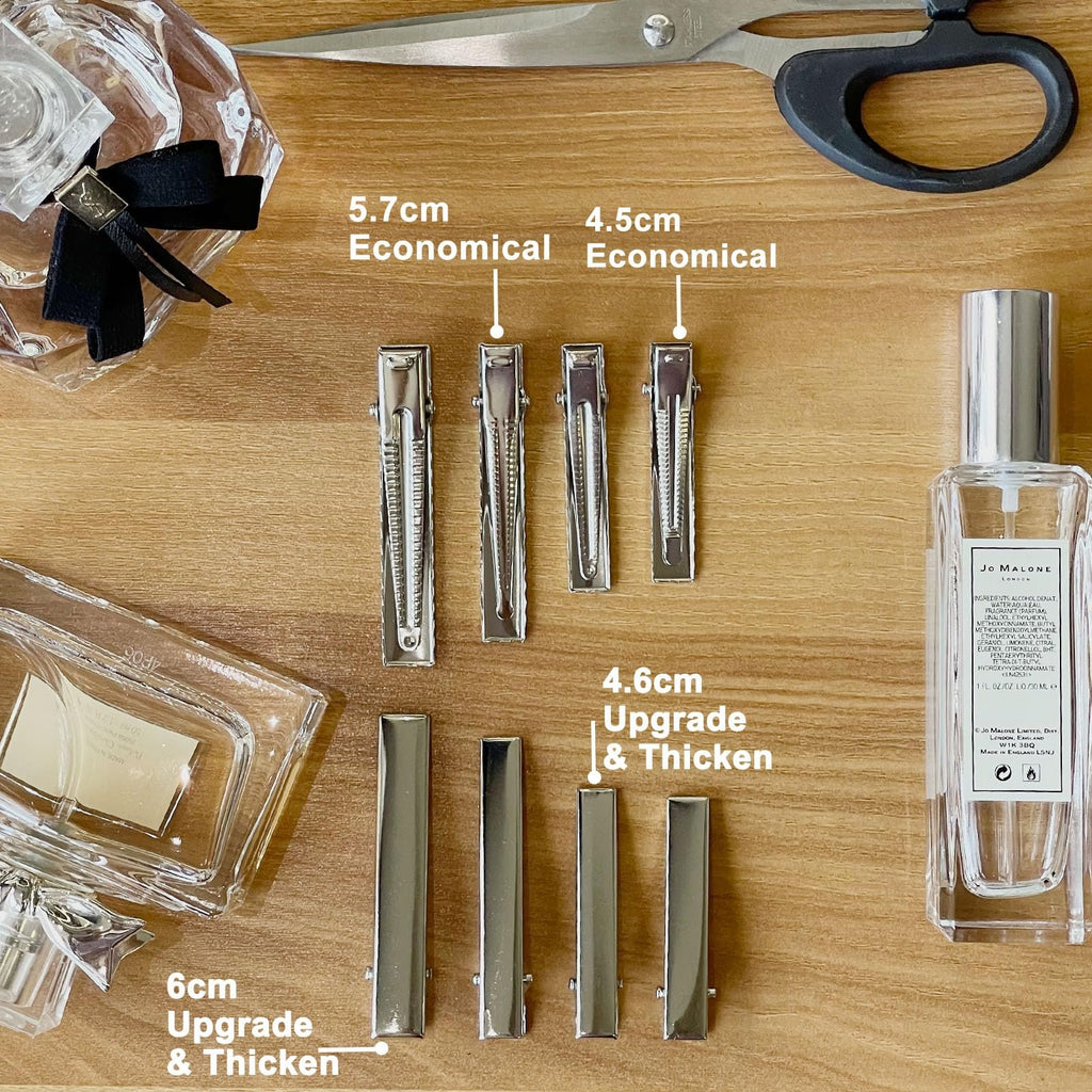 Various sizes of metal alligator hair clips laid out on a wooden surface with perfume bottles and scissors.