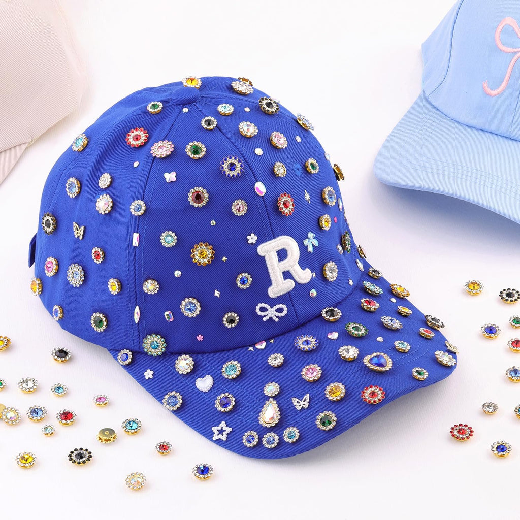 Blue baseball cap adorned with colorful rhinestones and charms, with loose rhinestones scattered around.