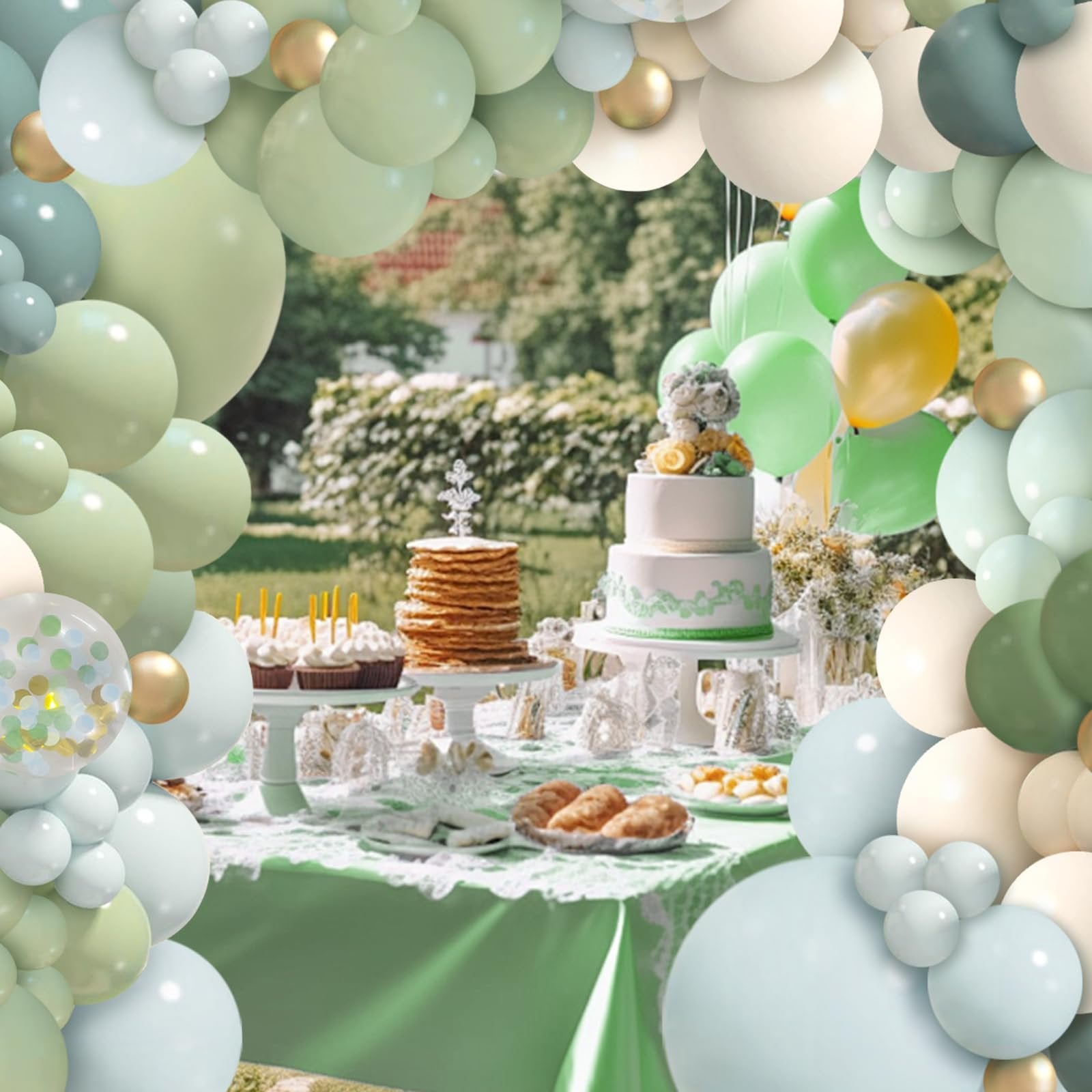 Dusty blue, green, and gold balloons framing a dessert table with a cake and cupcakes at an outdoor party.