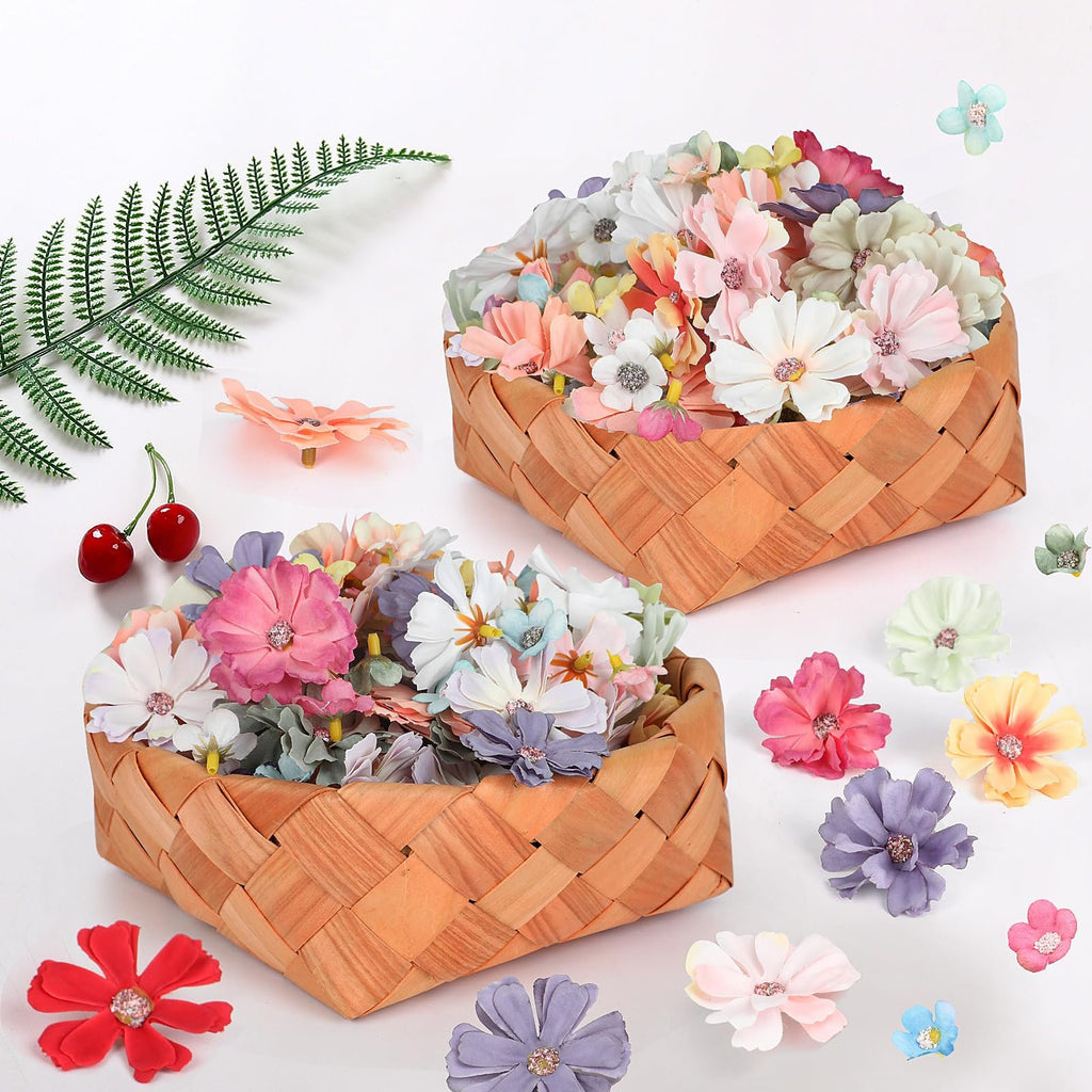 Two woven baskets filled with assorted faux fabric flowers, with scattered flowers and a fern sprig on a white background.