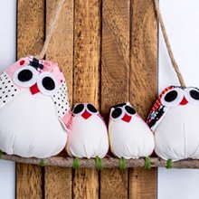 Four fabric owl ornaments hanging on a branch against a wooden background