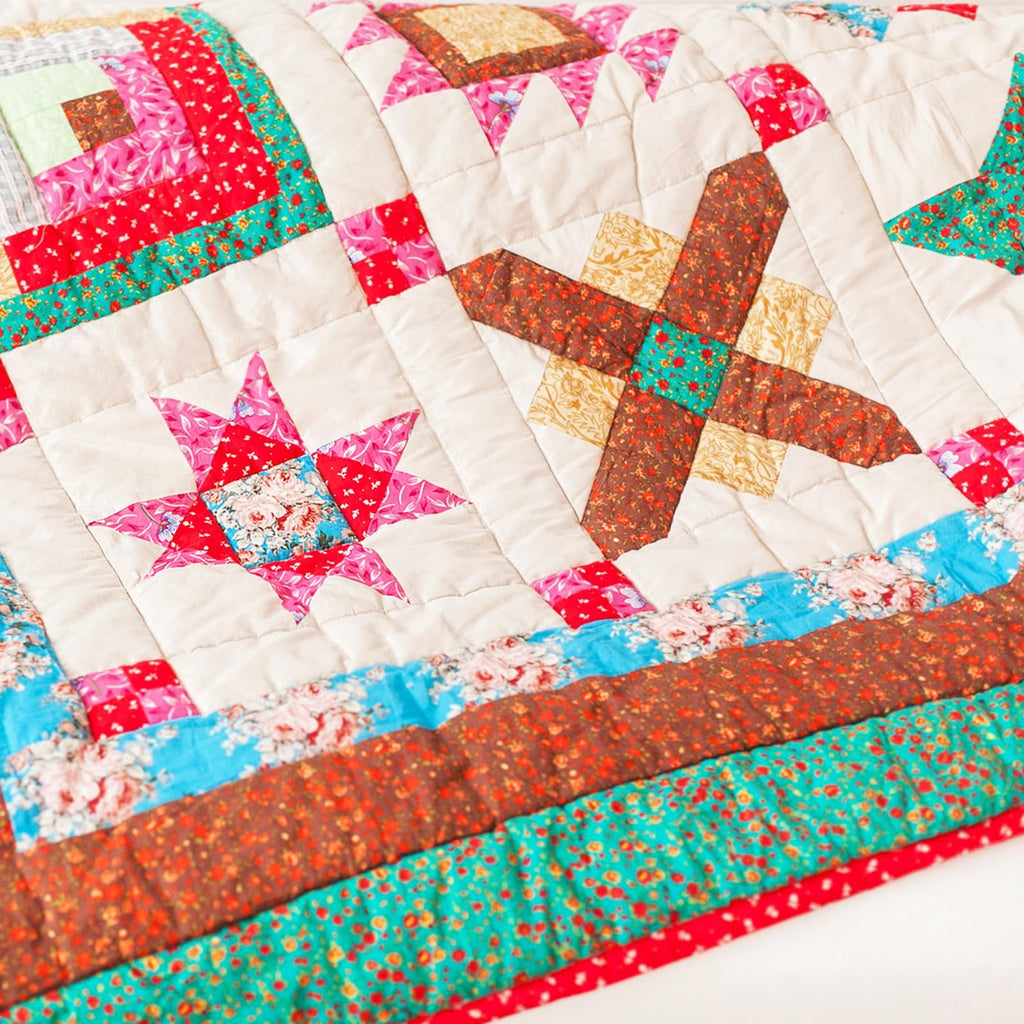 Close-up of a handmade quilt with various colorful fabric squares arranged in star and log cabin patterns, stitched together with white thread.