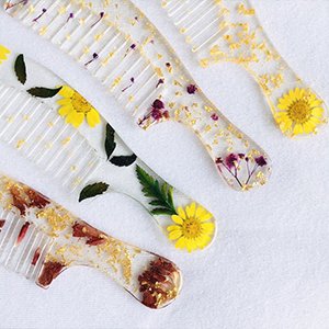 Four clear resin combs with embedded dried flowers and gold flakes, displayed on a white surface.