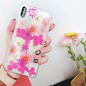 Clear phone case filled with dried pink and white flowers, held by a hand with decorated nails.
