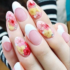 Close-up of hands with French manicured nails decorated with dried pressed flowers and small rhinestones.