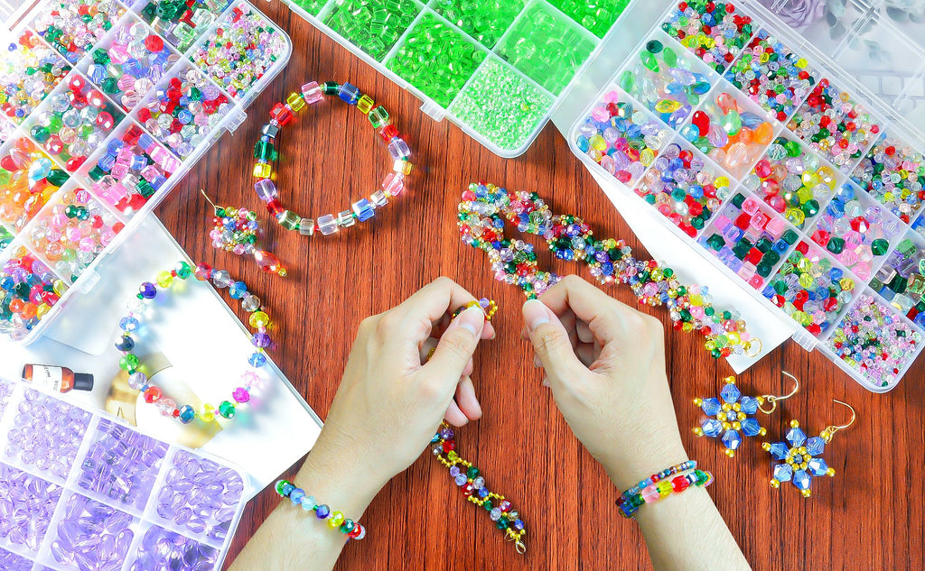 Hands assembling colorful crystal beads into jewelry, surrounded by organizer boxes of beads.