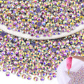 Pile of iridescent AB hotfix rhinestones with a pink applicator tool applying them to a surface in a star shape.