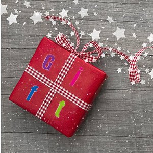 Red gift box wrapped with checkered ribbon, decorated with colorful letter stickers spelling 'Gift' and white stars on a wooden background.