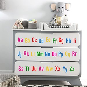 Colorful vinyl alphabet and number stickers applied to the drawers of a gray dresser in a nursery setting.