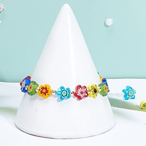 Handmade flower millefiori glass beads bracelet on white cone display, with loose beads scattered around.