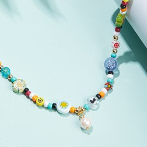 Handmade necklace with colorful millefiori glass beads and a pearl charm, displayed on a light blue surface with soft shadows.