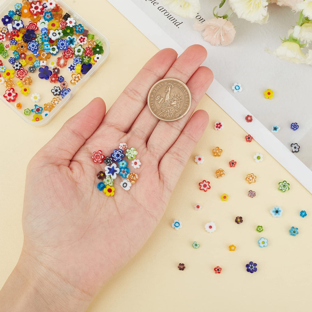 Hand holding assorted colorful flower millefiori glass beads next to a clear container of beads and a coin for scale.