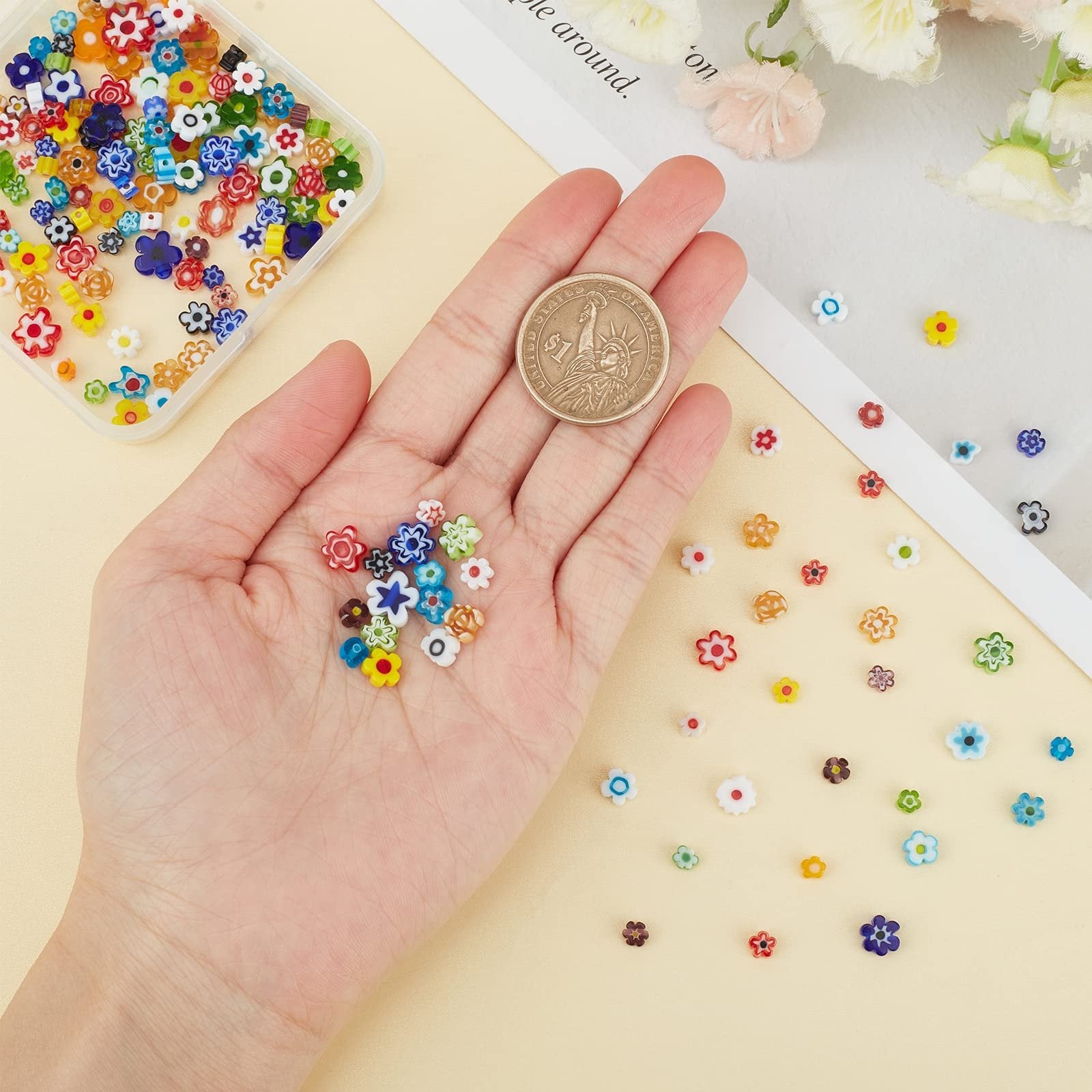 Hand holding assorted colorful flower millefiori glass beads next to a clear container of beads and a coin for scale.