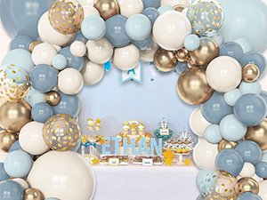 Dusty blue, white, and gold balloon arch over a party table with cupcakes and a name sign.