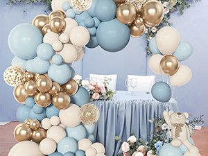 Dusty blue, white, and gold balloon arch with confetti balloons, set up over a decorated table with flowers and a teddy bear.