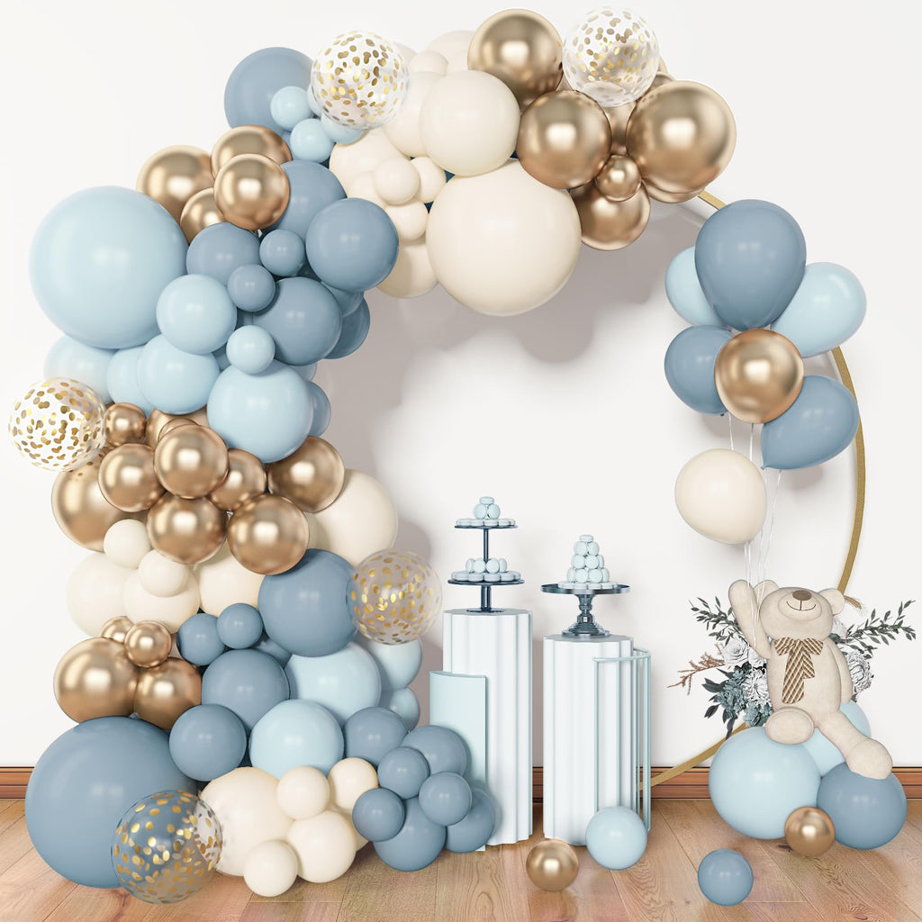 Dusty blue, white, and gold balloon arch with clear confetti balloons, a teddy bear, and dessert stands.