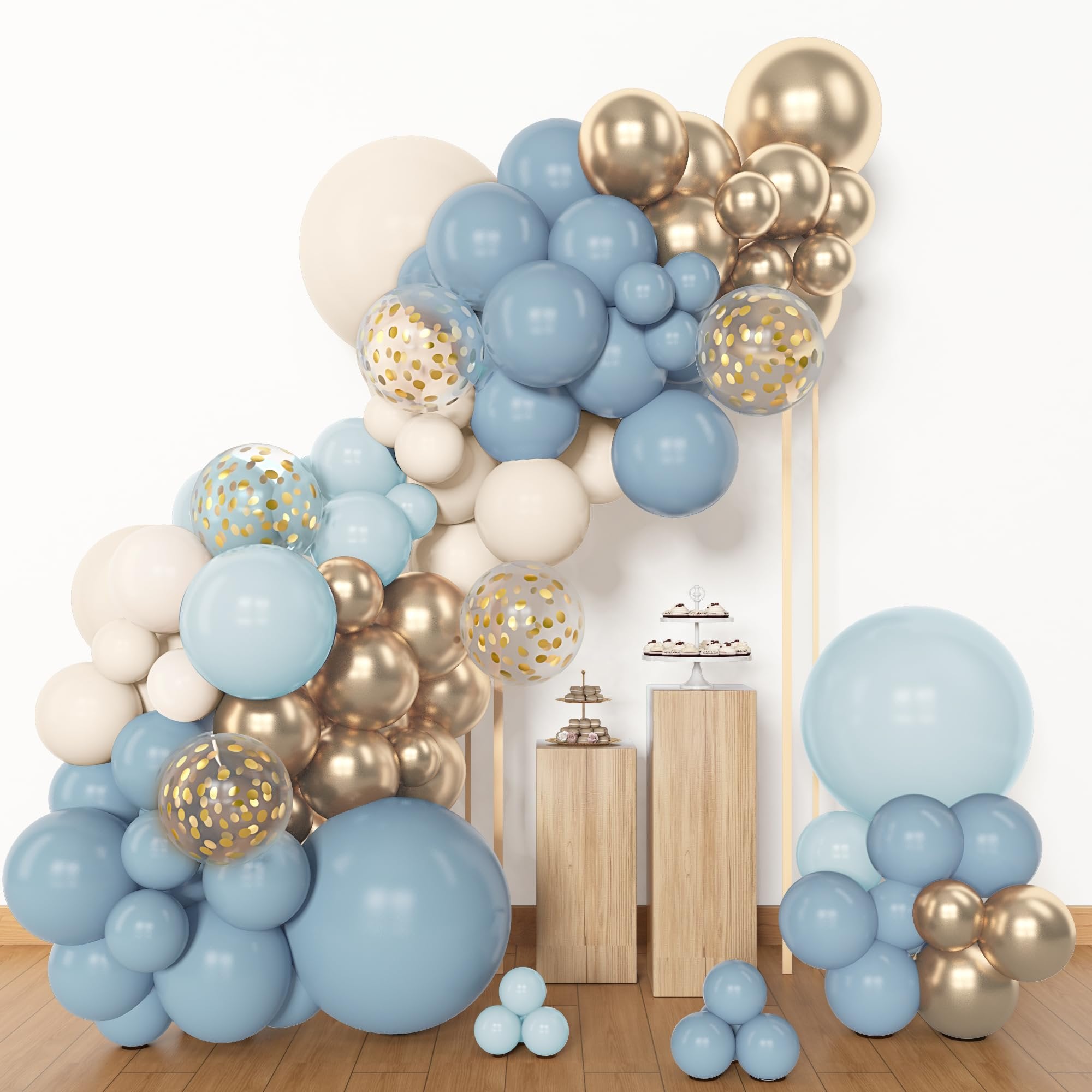 Dusty blue, white, and gold balloon arch with confetti balloons, displayed with cupcakes on wooden stands.