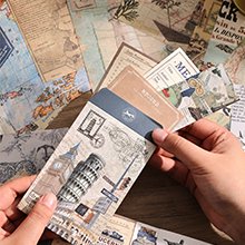 Hands holding a travel-themed scrapbook kit with stickers, papers, and journaling supplies.