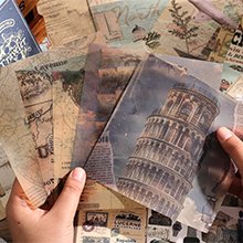 Hands holding various travel-themed scrapbook papers featuring maps and landmarks like the Leaning Tower of Pisa.