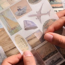 Close-up of hands holding a sheet of travel-themed stickers featuring airplanes, sailboats, and maps.