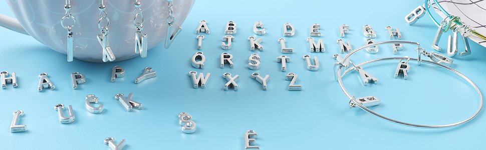 Antique silver alphabet letter charms scattered on a blue surface with a white mug and bracelet.