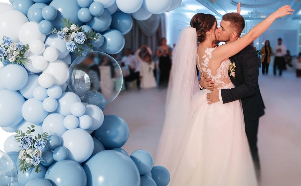 Dusty blue and white balloon arch with floral accents framing a kissing bride and groom at a wedding reception