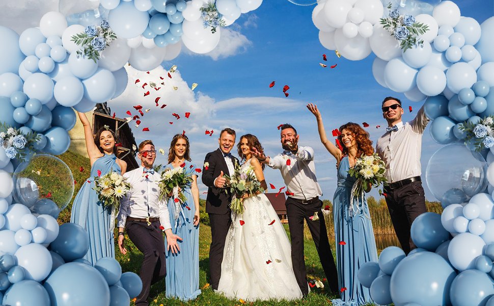 Wedding party celebrating under a dusty blue and white balloon arch with falling red petals