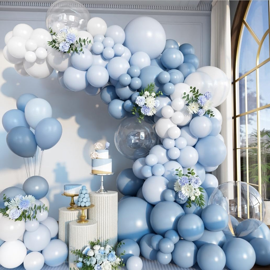 Dusty blue and white balloon arch with clear balloons, flowers, and cakes for a party decoration.