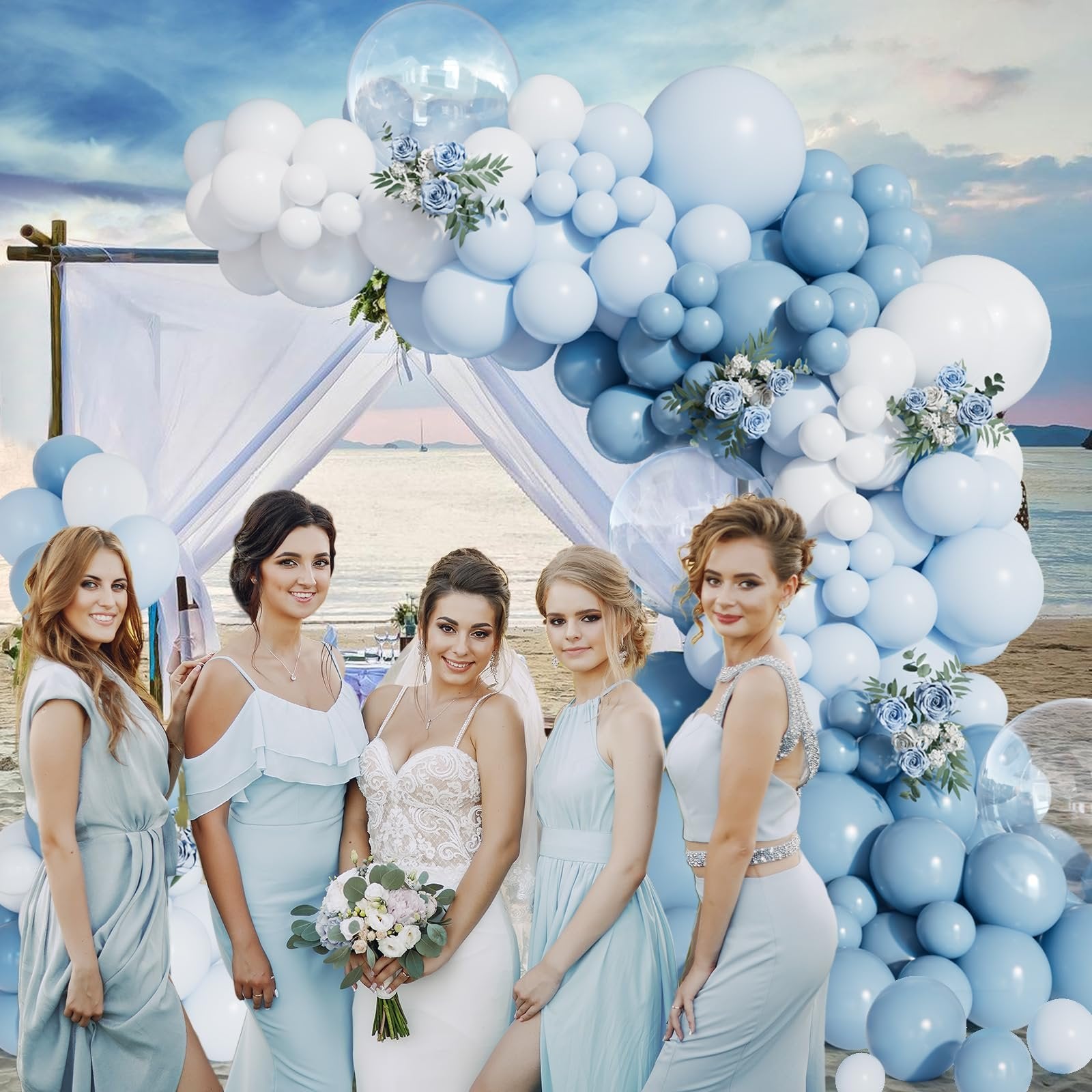 Bride and bridesmaids posing in front of a dusty blue and white balloon arch on a beach.