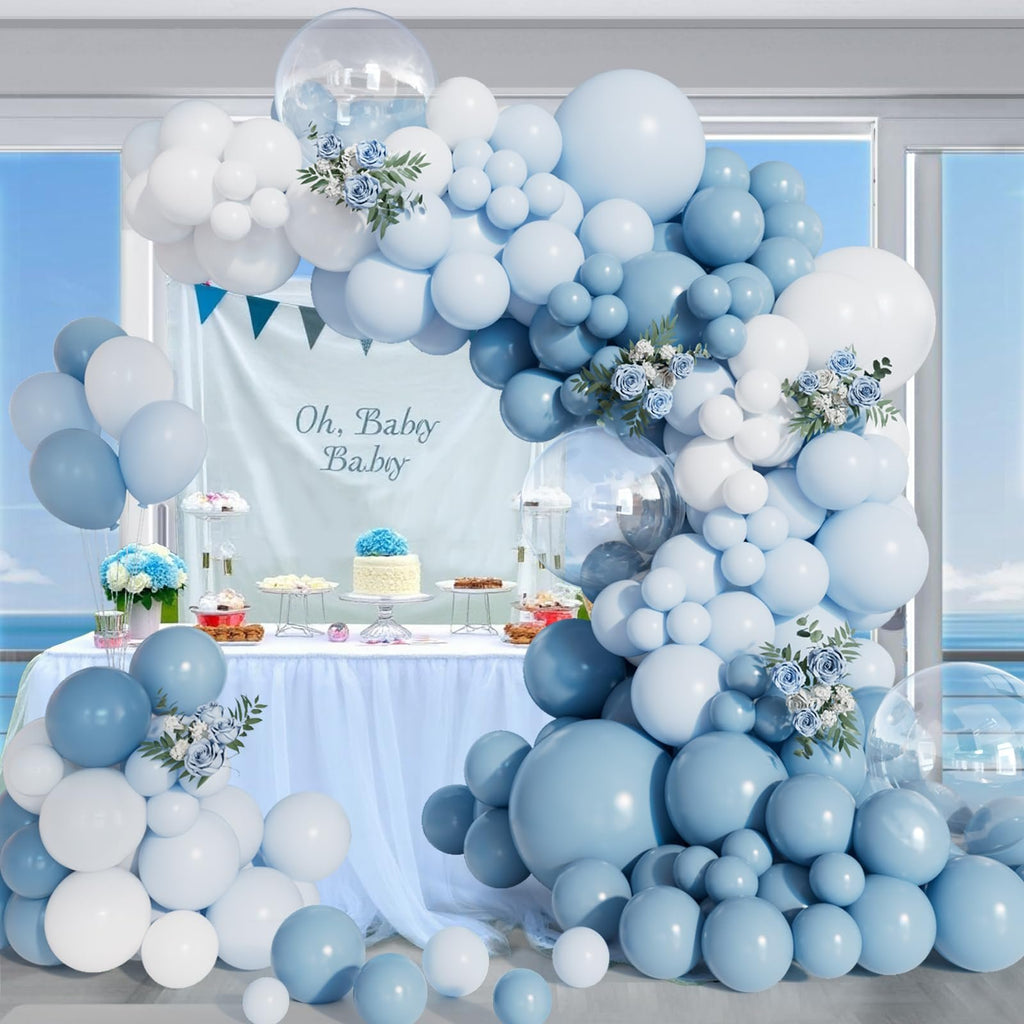 Dusty blue and white balloon arch with clear balloons and floral accents over a dessert table.