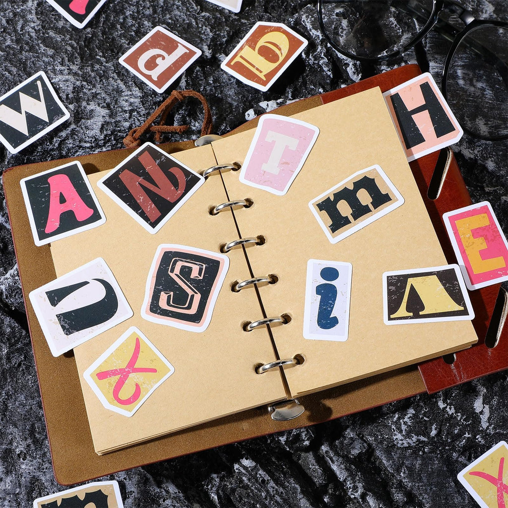 Retro alphabet stickers scattered on and around an open notebook, including letters A, N, S, T, H, E, W, D, and i.