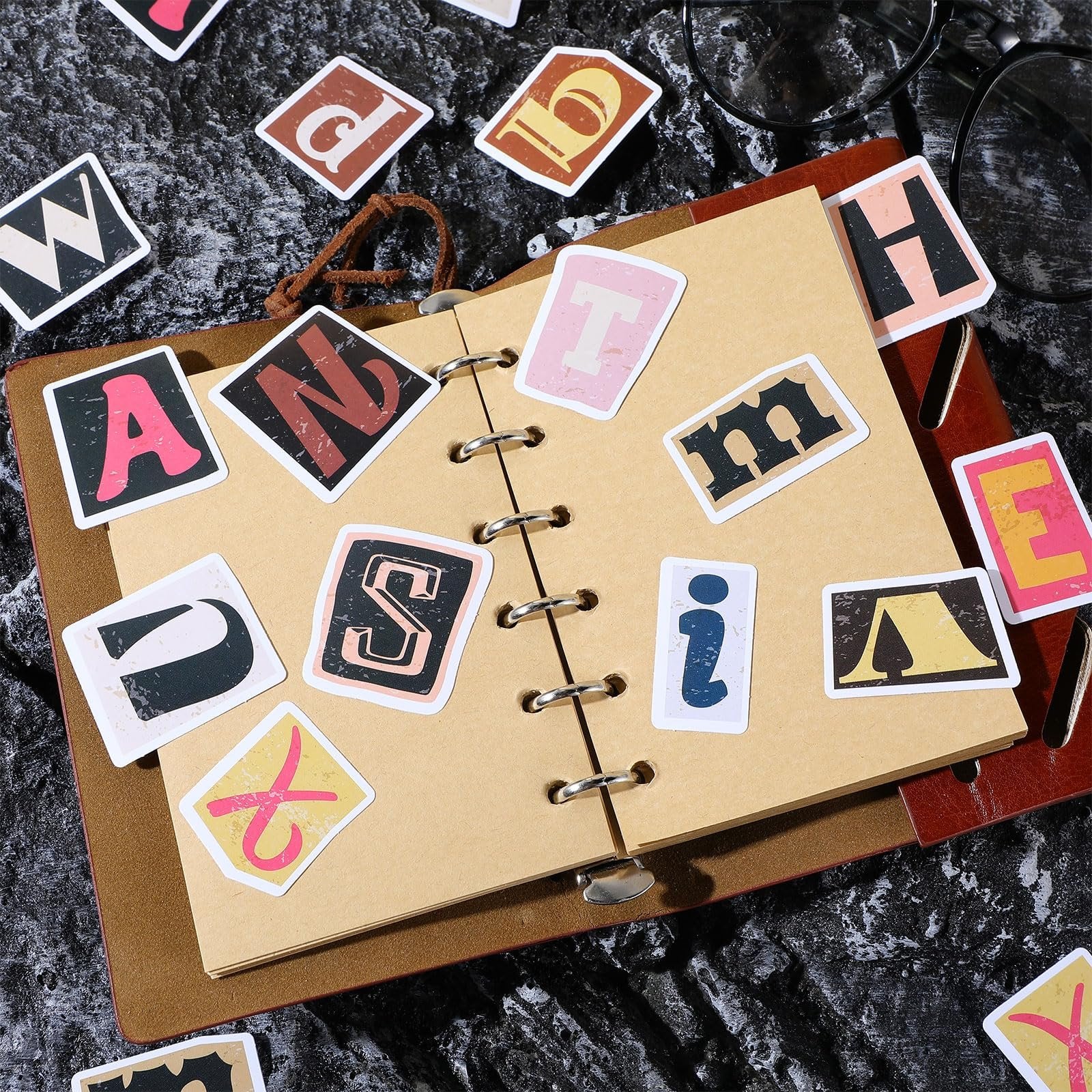 Retro alphabet stickers scattered on and around an open notebook, including letters A, N, S, T, H, E, W, D, and i.