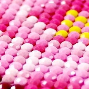 Close-up of a diamond painting kit with pink, white, and yellow faceted beads arranged in rows.