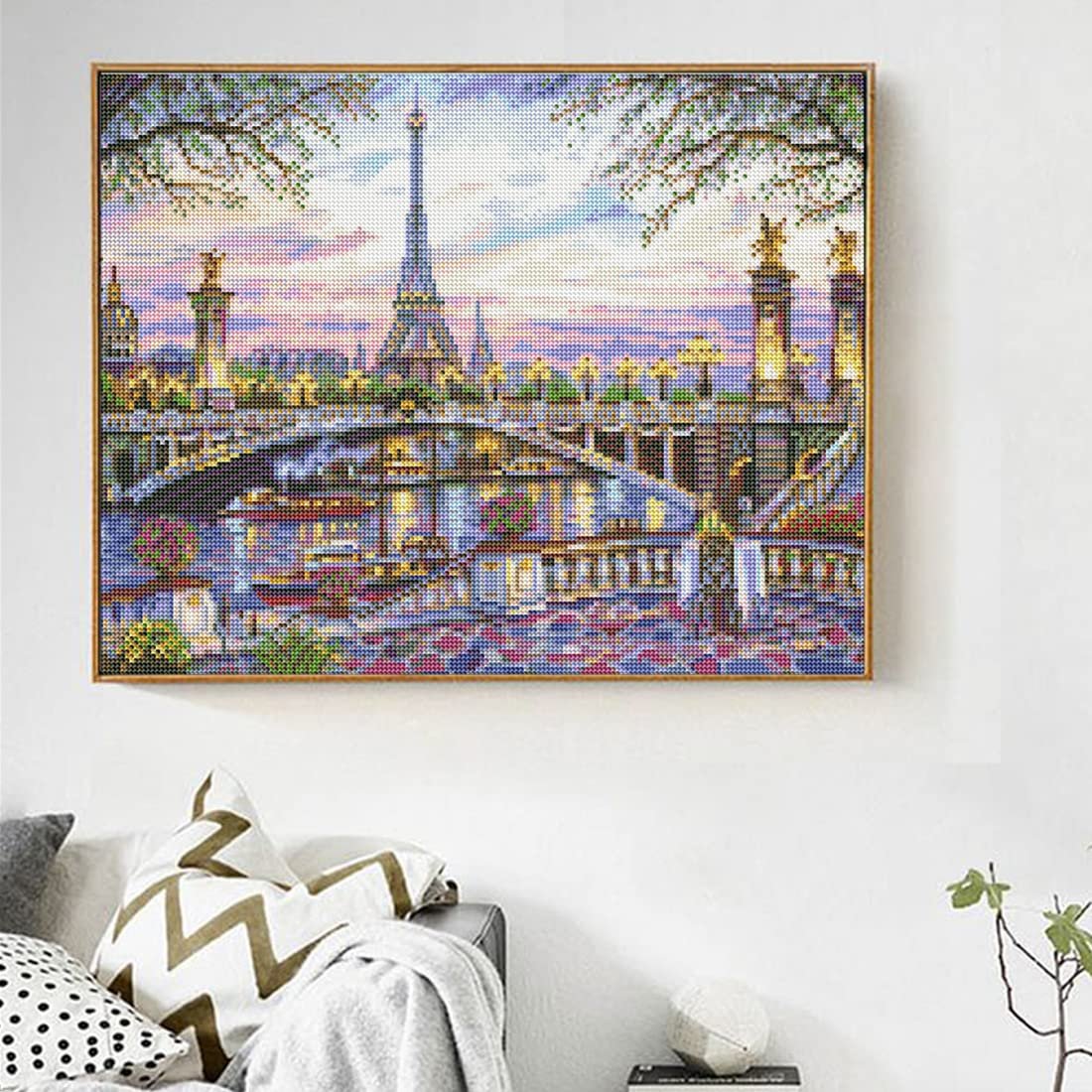 Diamond painting of Paris cityscape with Eiffel Tower and bridge at dusk, framed and hanging on a wall above a sofa.