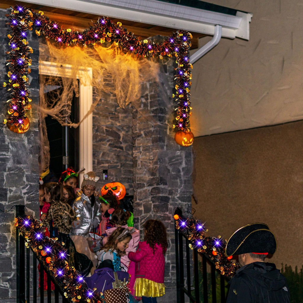 Halloween tinsel garland with purple LED lights and pumpkin accents decorating a house entrance with children in costumes.