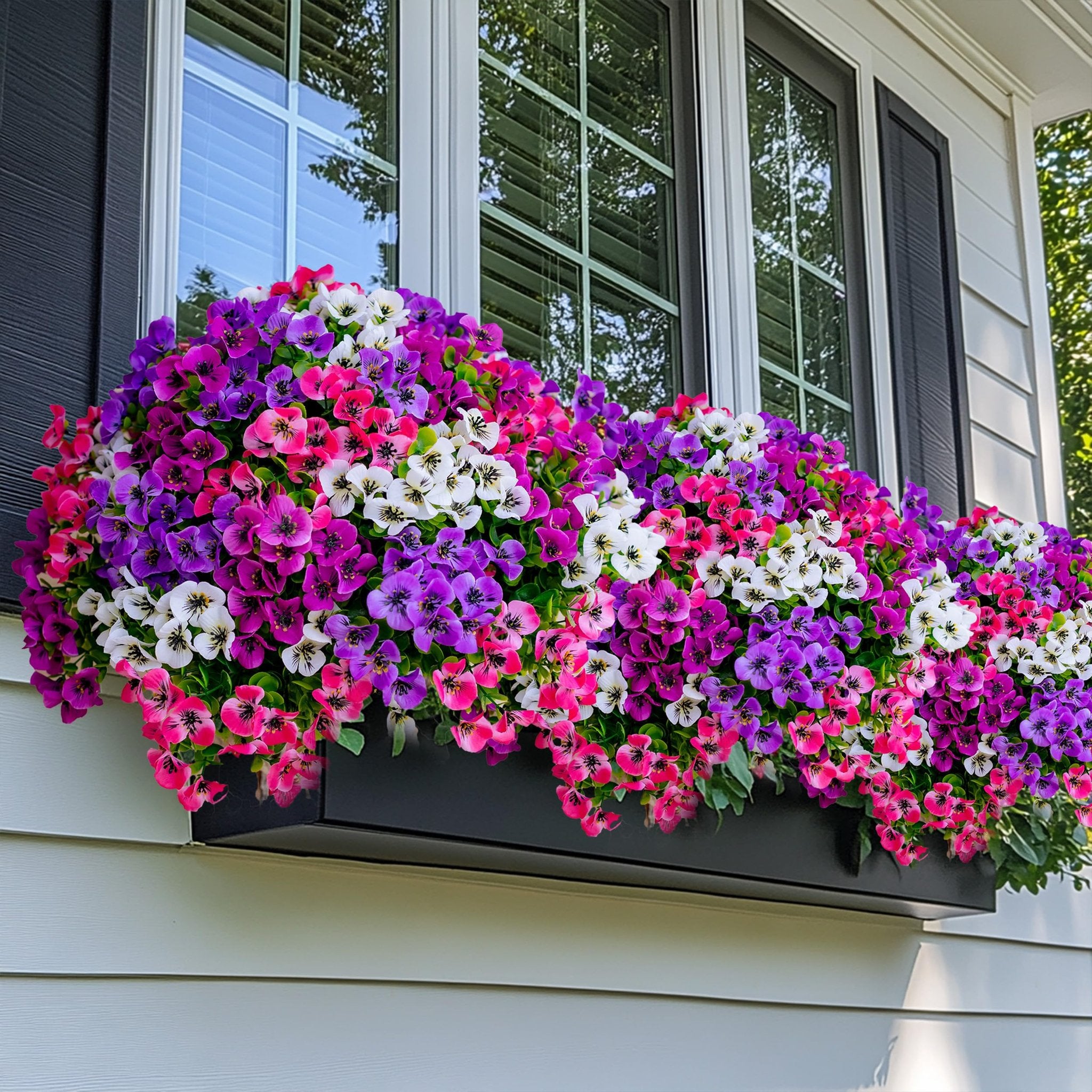 Window box filled with vibrant artificial flowers in shades of pink, purple, and white, set against a house exterior with shutters and windows.
