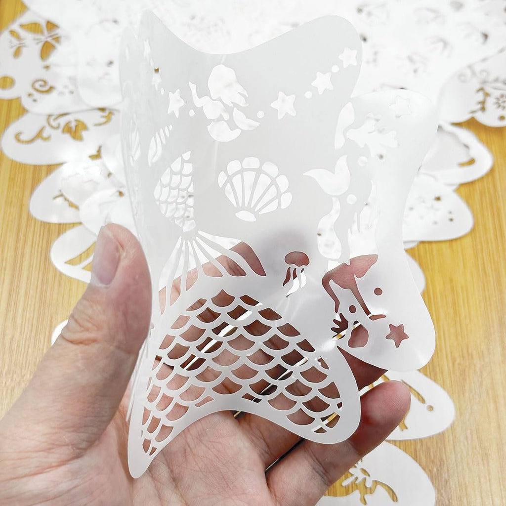 Hand holding a white mermaid-themed face paint stencil with various sea creature cutouts.