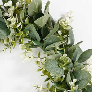 Close-up of an artificial eucalyptus leaves garland with small white flowers on a white background.