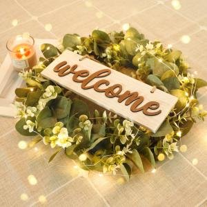 Artificial eucalyptus leaves wreath with a wooden 'welcome' sign and fairy lights