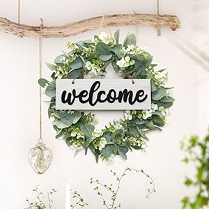 Artificial eucalyptus leaves wreath with white flowers and a black 'welcome' sign hanging on a driftwood branch.