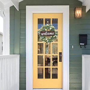 Artificial eucalyptus leaves wreath with a 'welcome' sign hanging on a yellow front door.