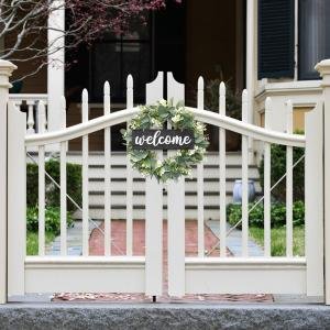 Artificial eucalyptus leaves wreath with a black welcome sign hangs on a white garden gate.