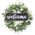 Artificial eucalyptus leaves wreath with white 'welcome' sign hanging on a white background