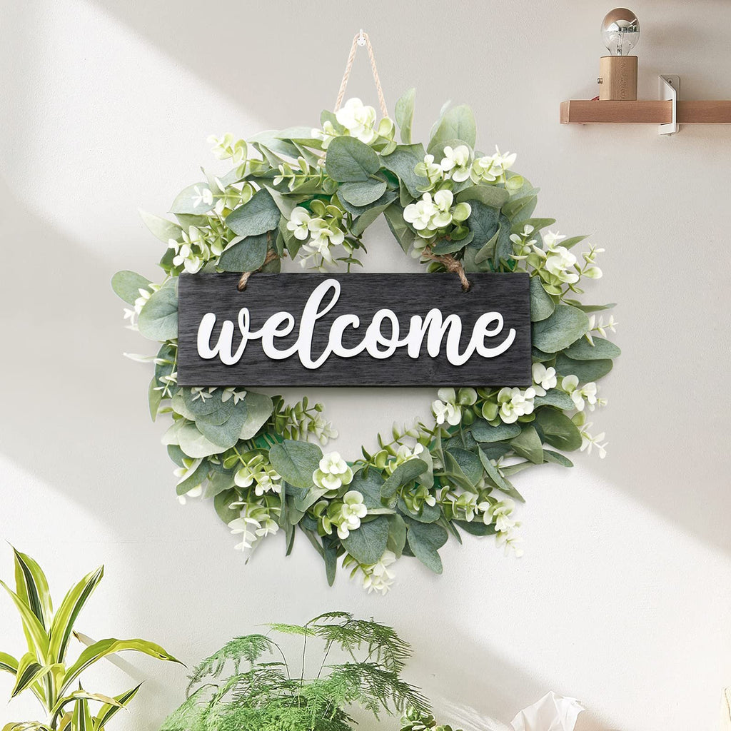Artificial eucalyptus leaves wreath with white 'welcome' sign hanging on a wall with plants below