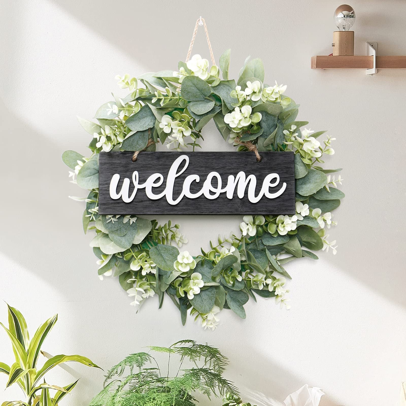 Artificial eucalyptus leaves wreath with white 'welcome' sign hanging on a wall with plants below