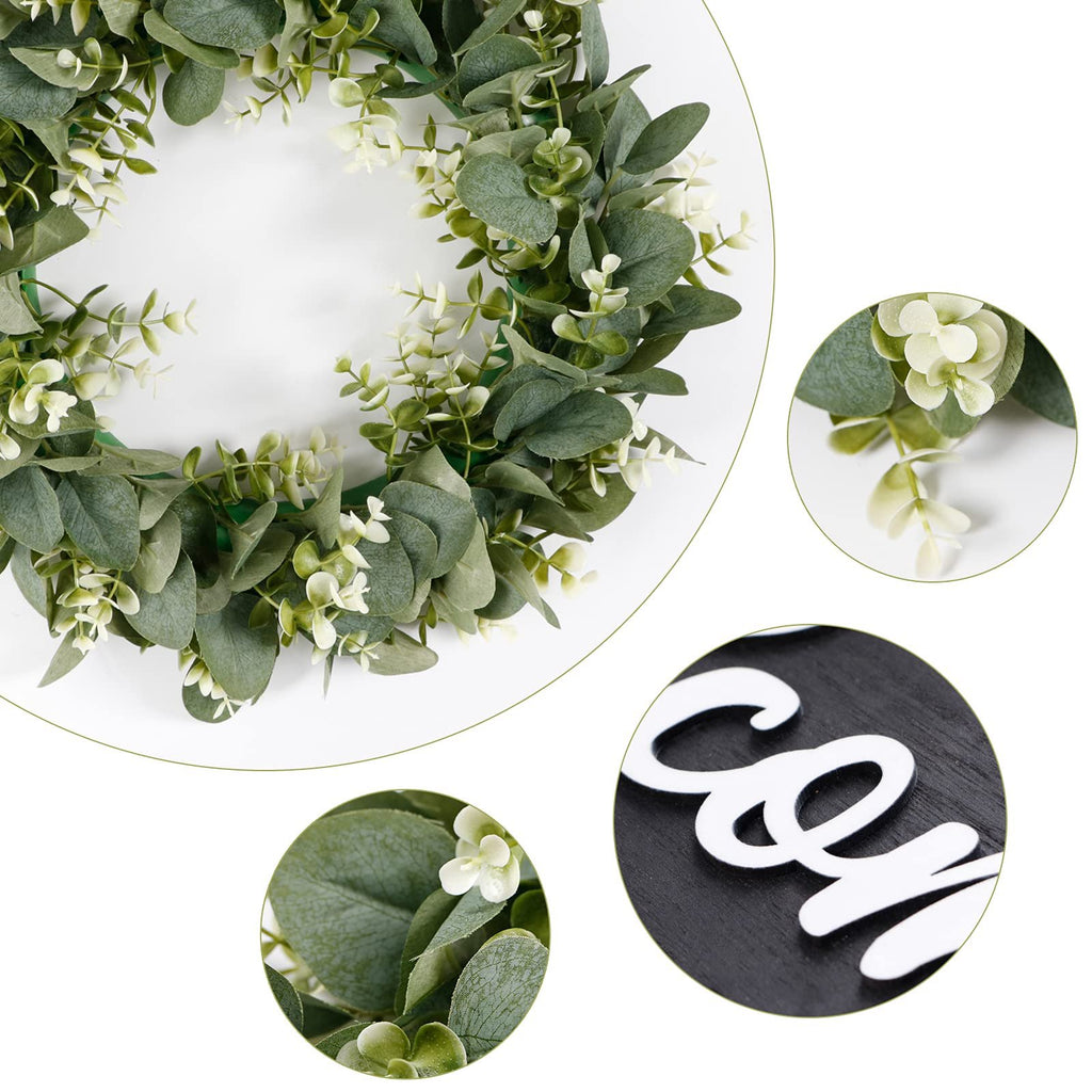Artificial eucalyptus wreath with small white flowers and a black sign board with white text reading 'Welcome'